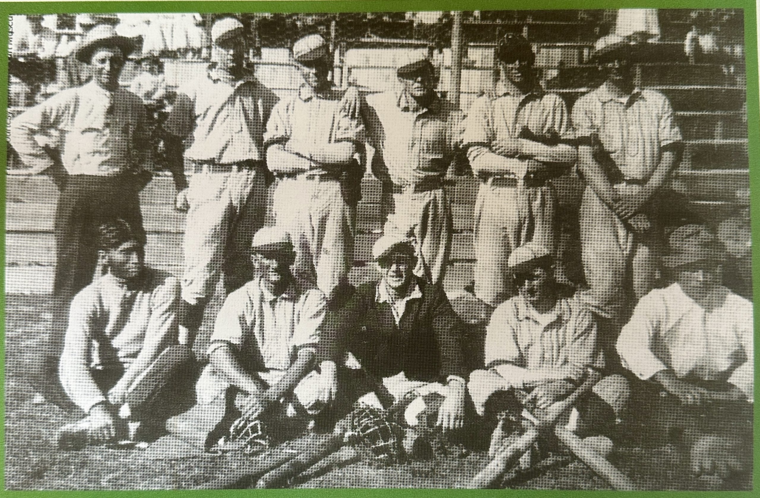 A vintage black-and-white grain photograph of a historic baseball team posed in two rows on a field. The players wear period-accurate uniforms and caps, with wooden bats and catcher’s gear resting on the grass in the foreground.