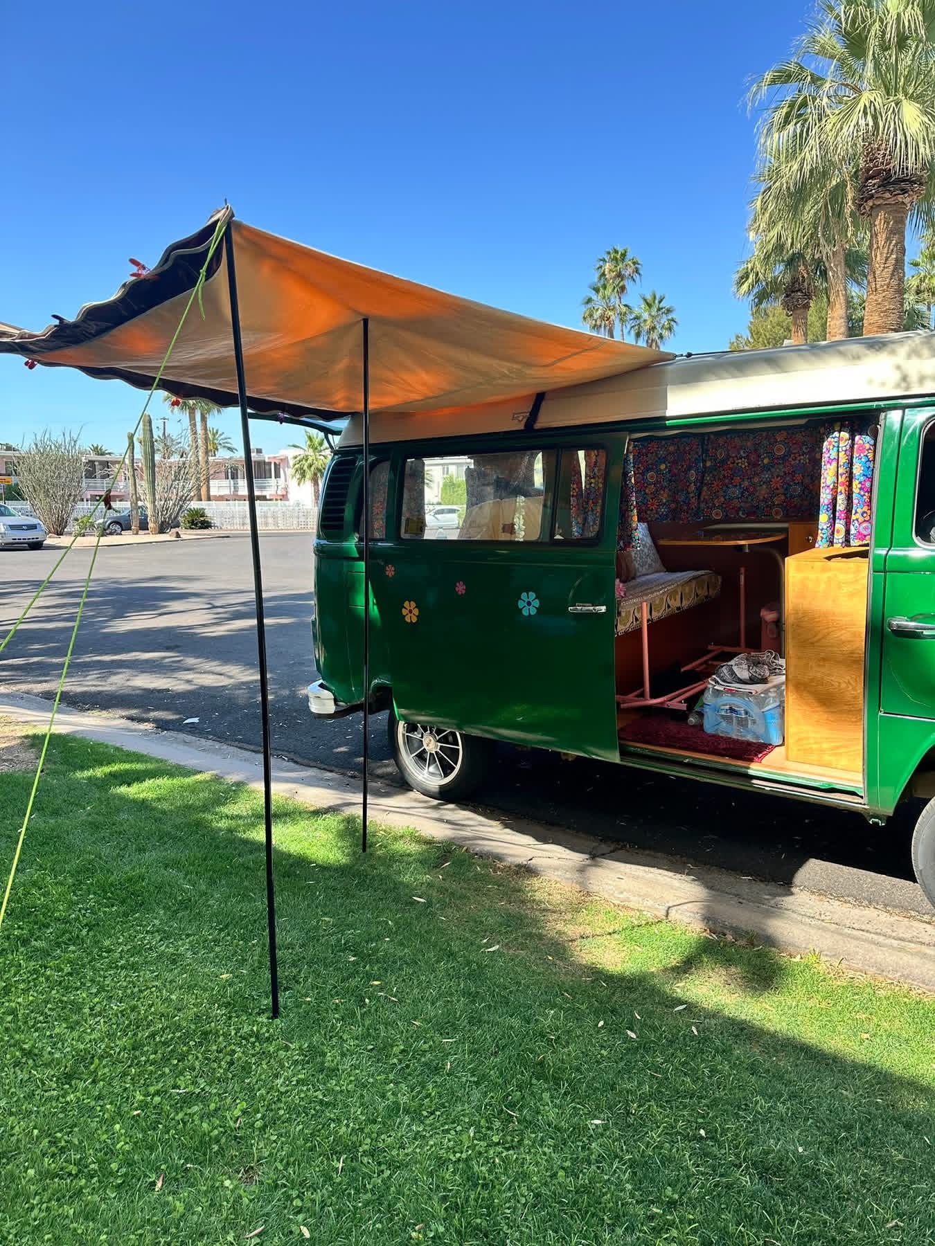 A Sumatra Green 1973 Westfalia VW Bus with original awning set up on green grass.