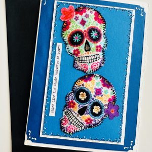 Hand-stitched sugar skull motif on vibrant cardstock.