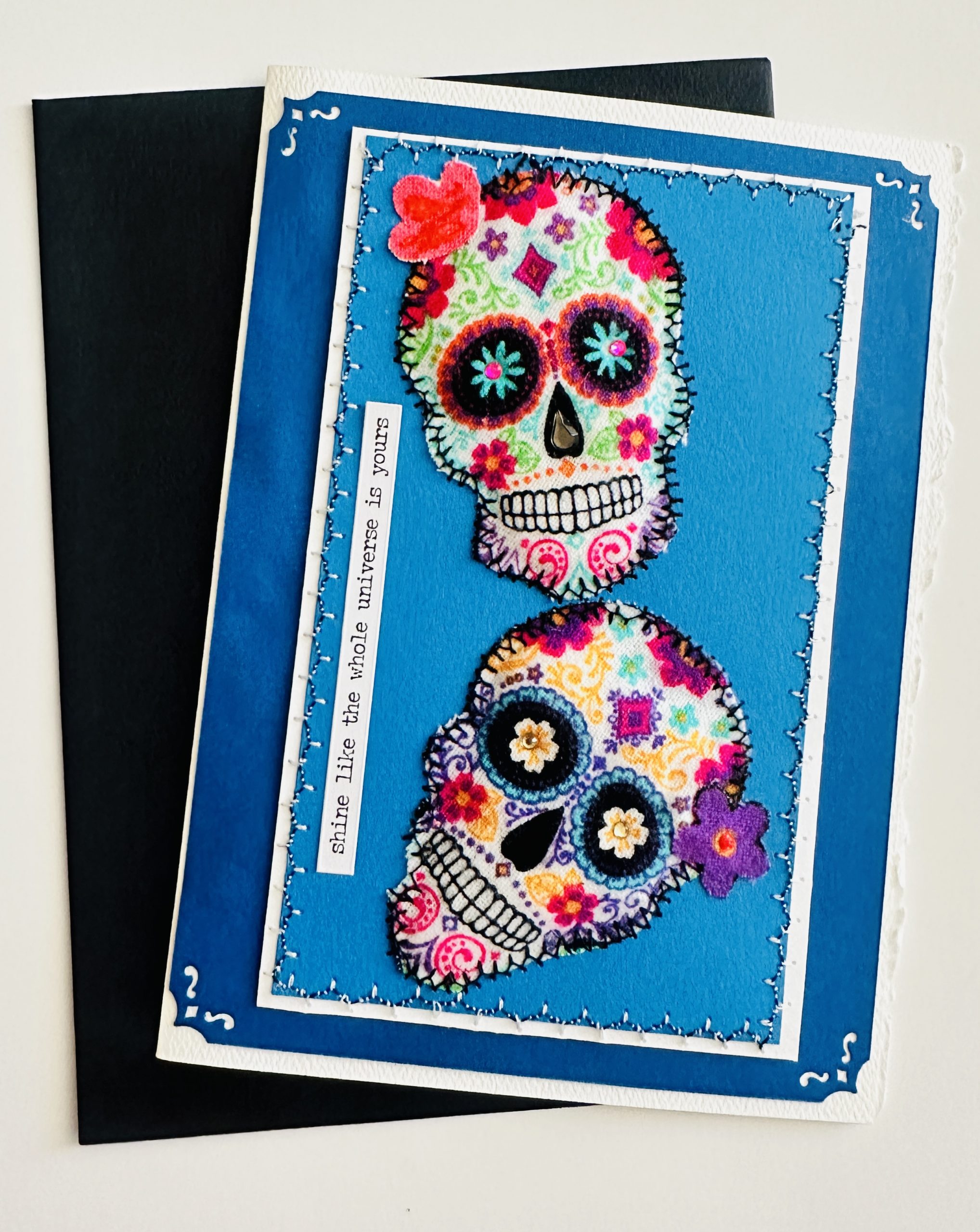 Hand-stitched sugar skull motif on vibrant cardstock.