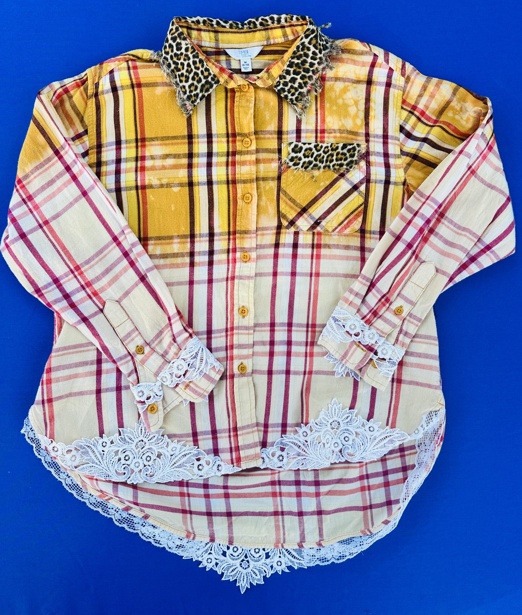 Close up of white vintage lace detailing on the cuff and hem of a hand-bleached yellow plaid flannel shirt.