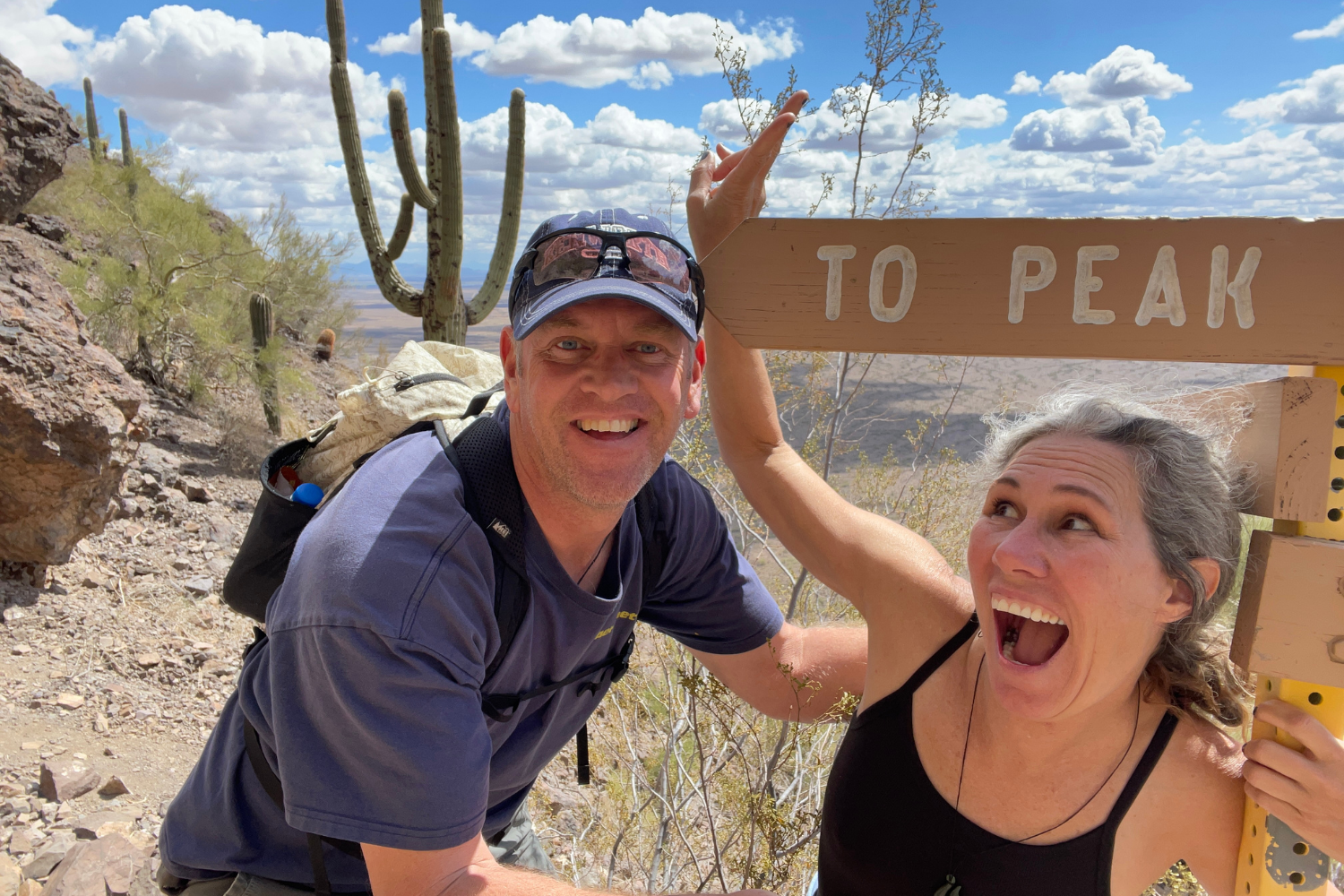 Heather laughing wildly next to a trail sign with Chris while hiking near a saguaro cactus at Picacho Peak.