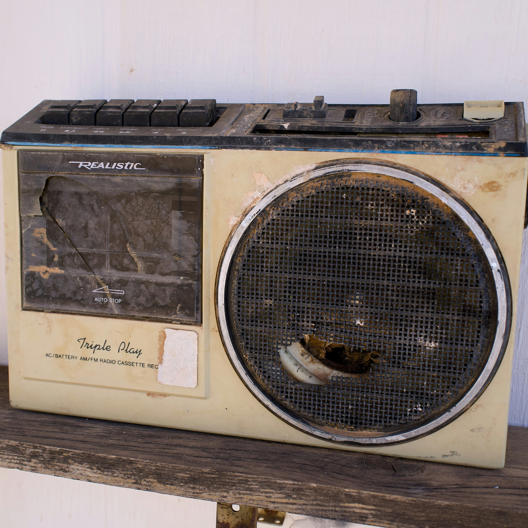 Close-up of a weathered, vintage 1970s portable AM/FM transistor radio with a metallic speaker grille and tuning dial, set against a dark rustic backdrop.